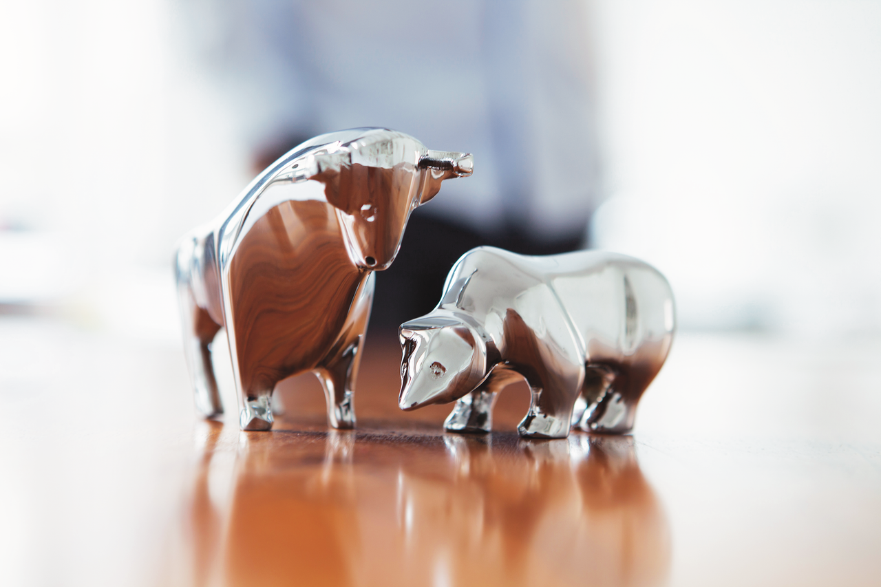 Zwei silberne Figuren von Bulle und Bär stehen auf einer glänzenden Holzoberfläche, Symbol für die Entwicklung an der Börse.